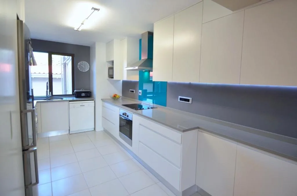 Modern galley kitchen with white cabinetry, stainless steel appliances, and turquoise backsplash