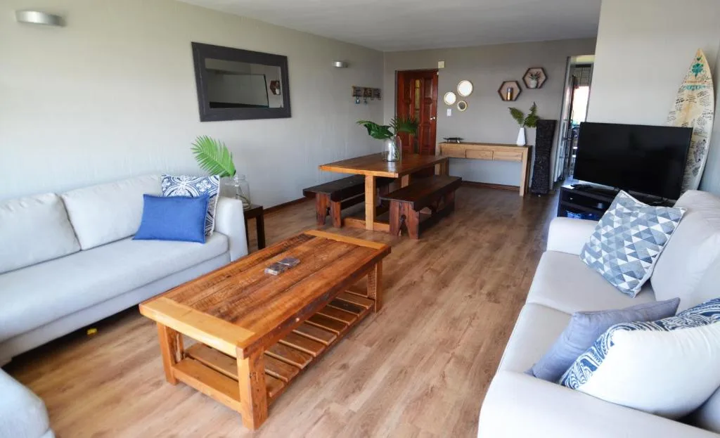 Spacious open-plan lounge with white sofas, wooden coffee table, and TV