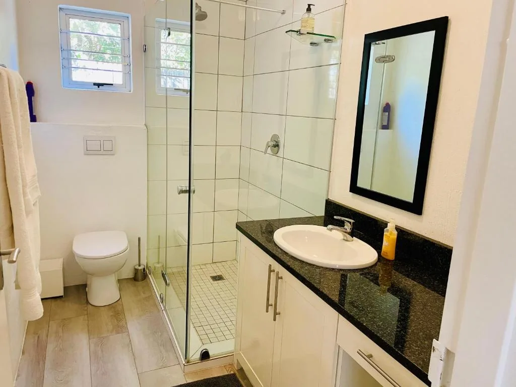 Modern bathroom with glass shower, white toilet, black vanity counter and framed mirror