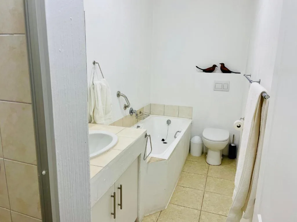 Clean bathroom with vanity sink, bathtub, toilet, and decorative bird artwork