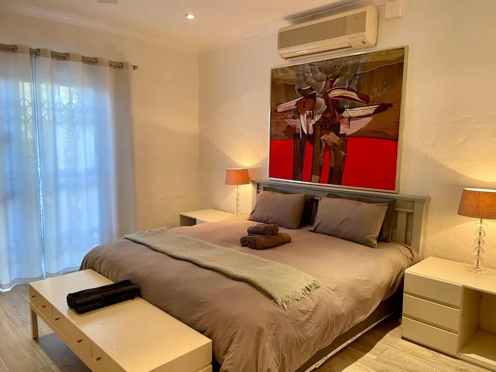 Spacious modern bedroom with queen bed, contemporary artwork, air conditioning unit, and garden views