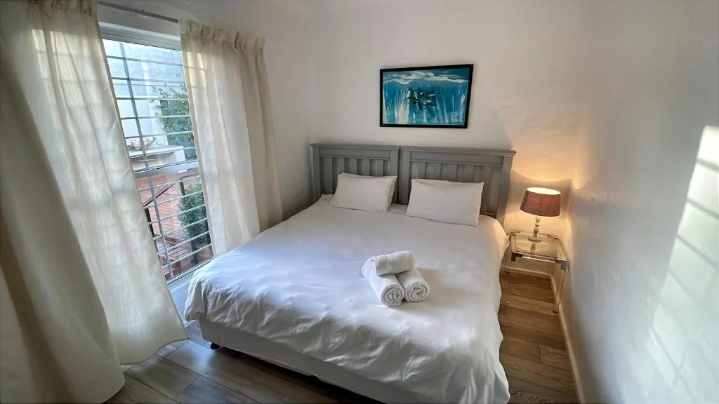 Bright bedroom with double bed, white bedding, and ocean view balcony access