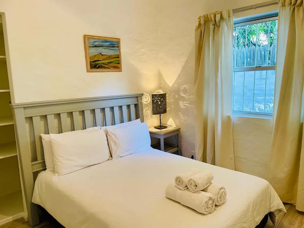 Bright bedroom with white bedding, rolled towels, and garden view through window