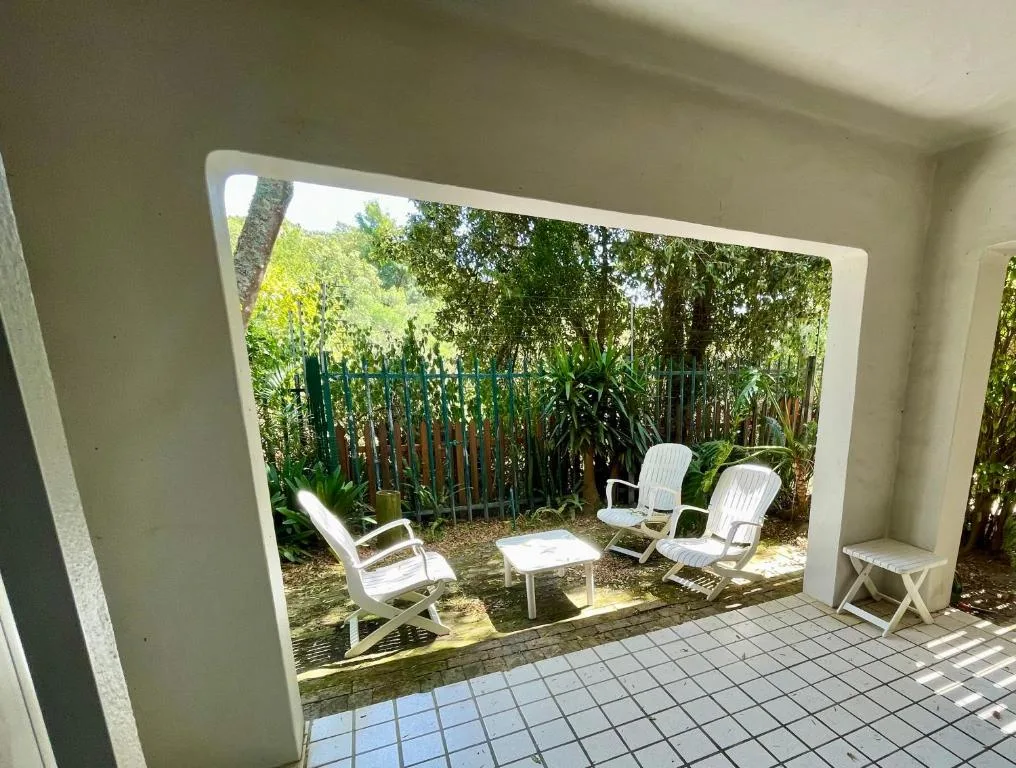 Shaded patio with white loungers and small table overlooking lush garden