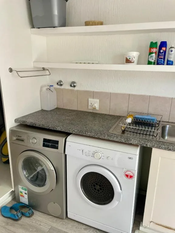 Compact laundry room with two washing machines and granite countertop shelving