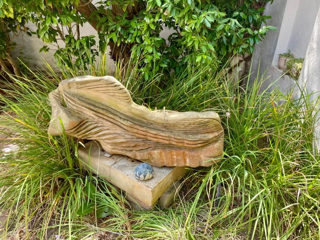 Carved wooden fish sculpture nestled among lush green plants in garden