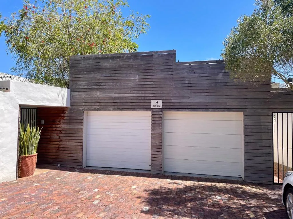 Modern dark wood facade with double garage doors and brick driveway entrance