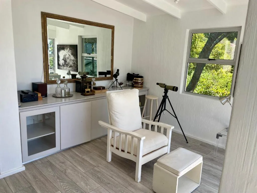 Bright lounge with white armchair, vanity desk, and telescope by window overlooking trees