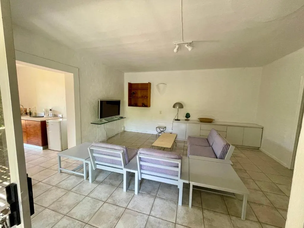 Bright living room with white furniture, TV, and kitchen view beyond