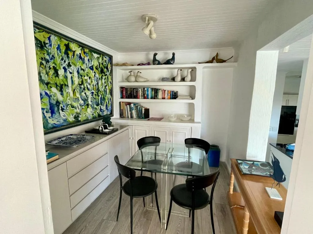 Modern lounge area with glass dining table, black chairs, and wall shelving