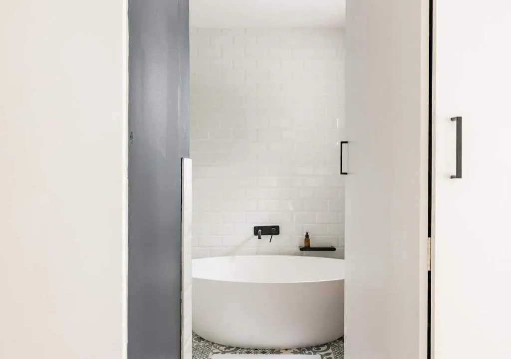 Modern white freestanding bathtub with black fixtures and tiled surround
