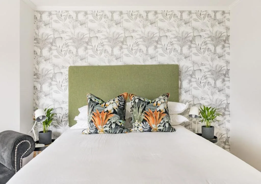 Bedroom with green headboard, patterned wallpaper, and colorful decorative pillows