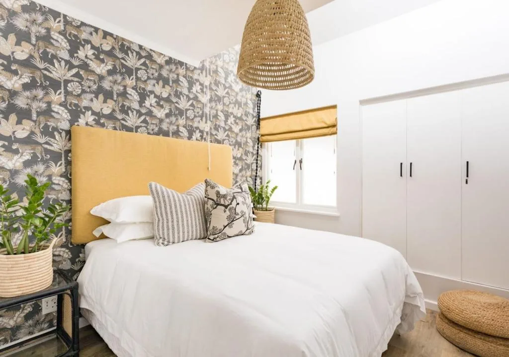 Bright bedroom with mustard headboard, floral wallpaper, and woven pendant lamp