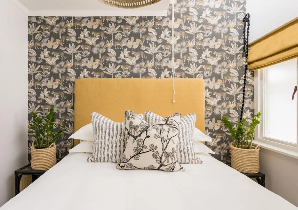 Bed with mustard headboard, patterned pillows, botanical wallpaper accent wall