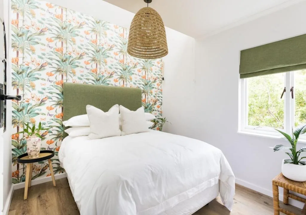 Bright bedroom with tropical wallpaper, green headboard, white bedding, and woven pendant light
