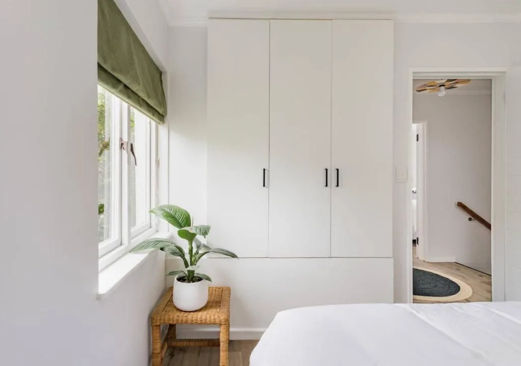 Bright bedroom with white built-in wardrobes and potted plant by window