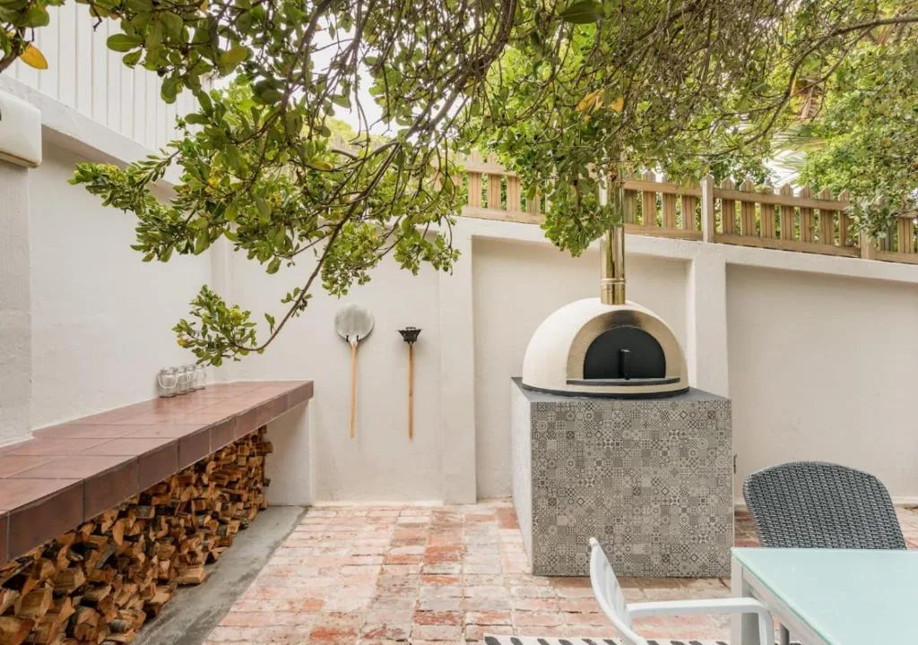 Outdoor patio with pizza oven, wood storage, and shaded seating area