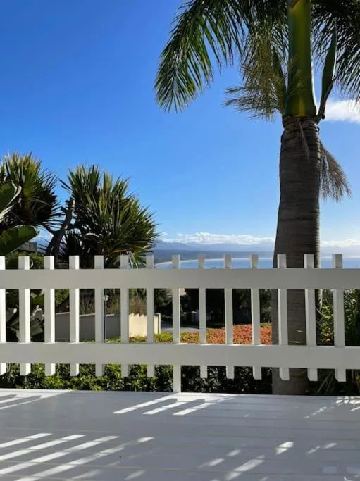 White railings and palm trees frame ocean and mountain views from the deck