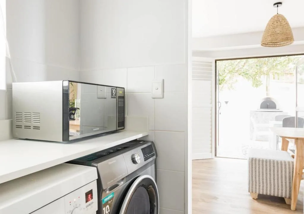 Microwave and washing machine in modern white utility laundry area