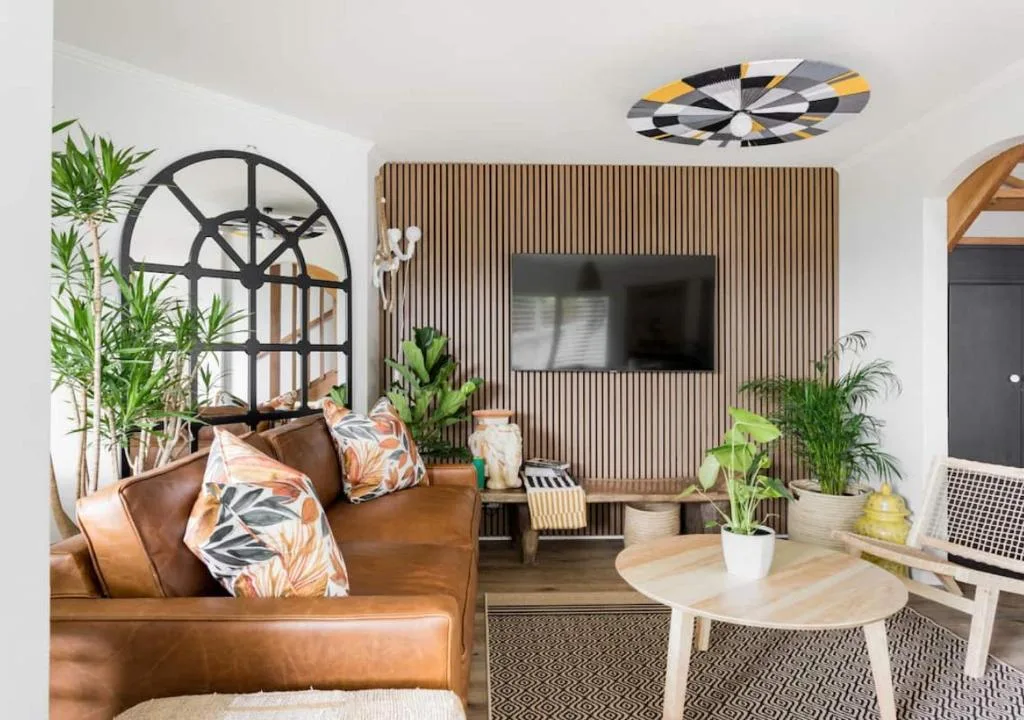 Modern living room with brown leather sofa, TV wall, plants, and contemporary decor