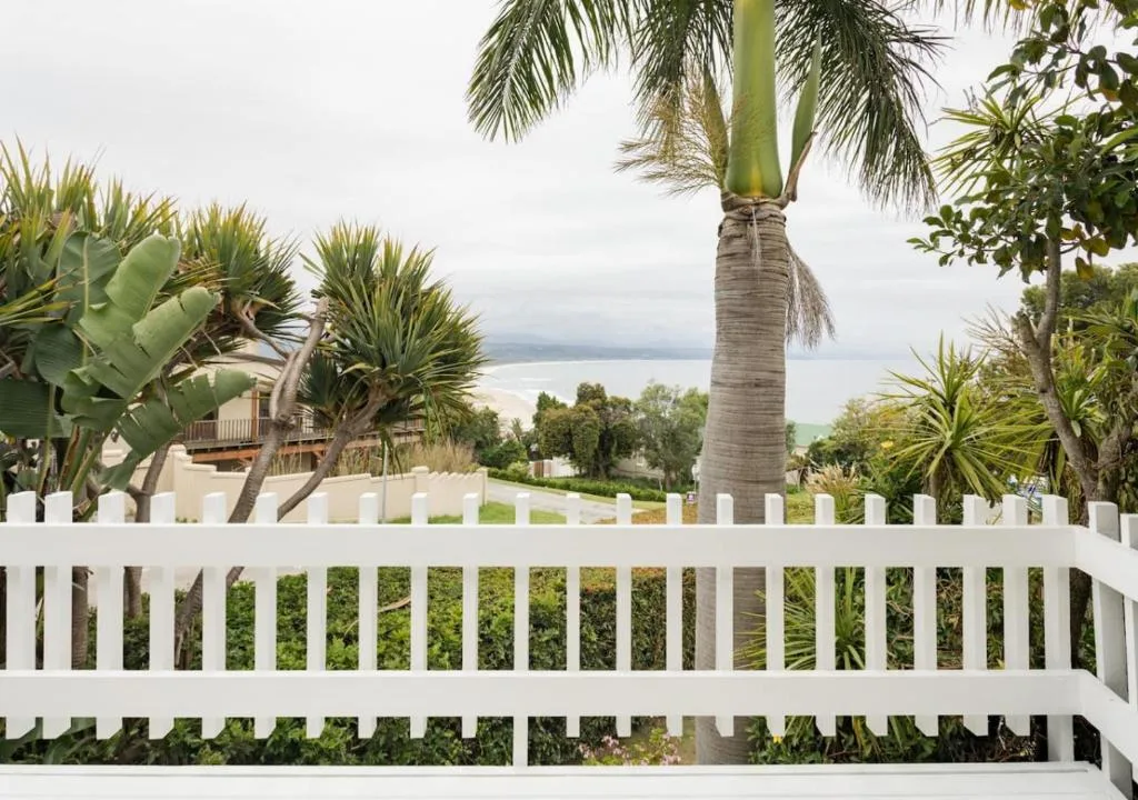 Lagoon and mountains visible through palm trees from white fence