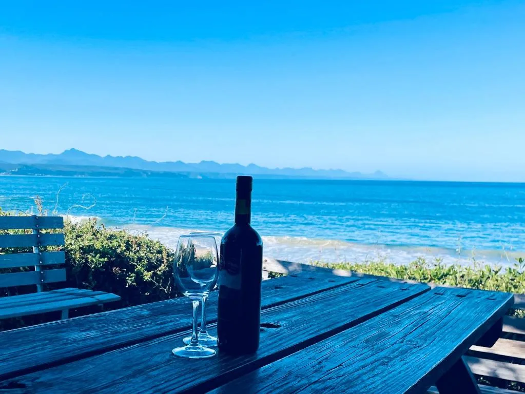 Wooden deck with wine bottle and glass overlooking ocean and mountains