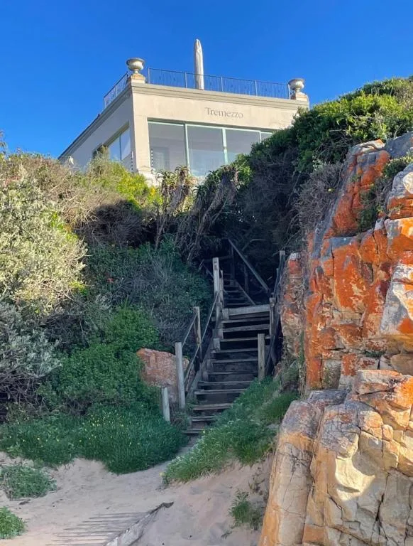 Modern beachfront villa with wooden stairs and natural rock formations leading up to entrance