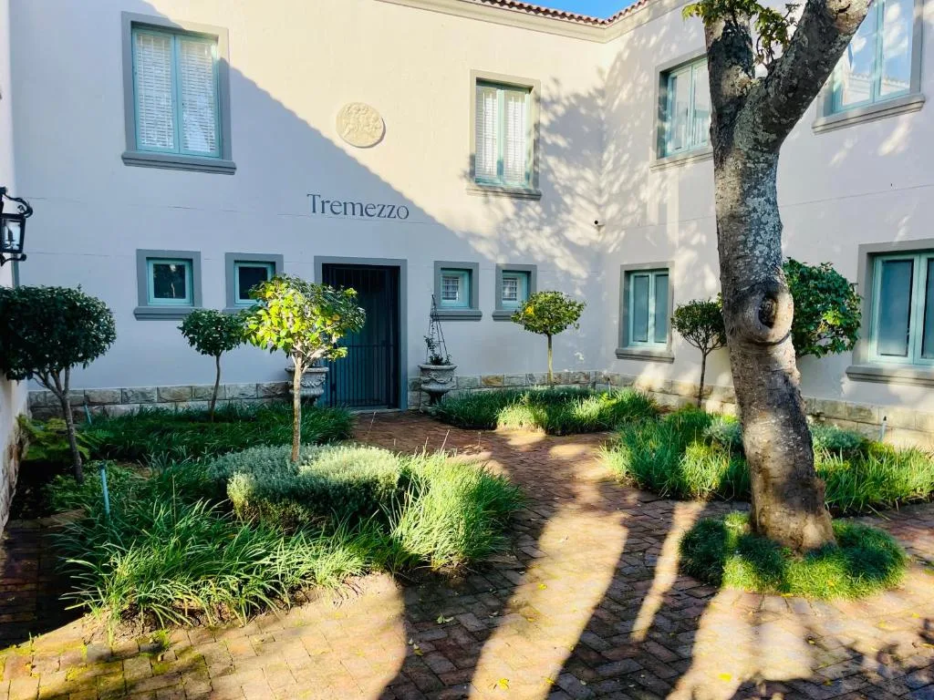 White villa facade with blue-trimmed windows, manicured garden, and mature tree