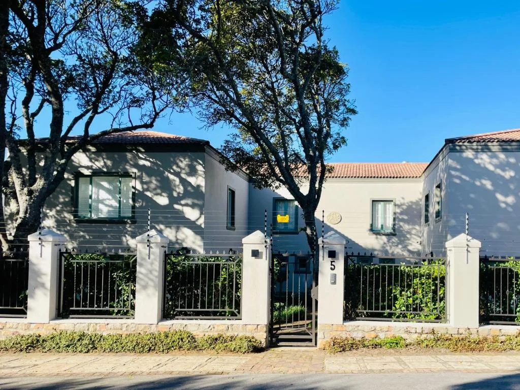 Modern white villa with black iron gates and mature trees overhead