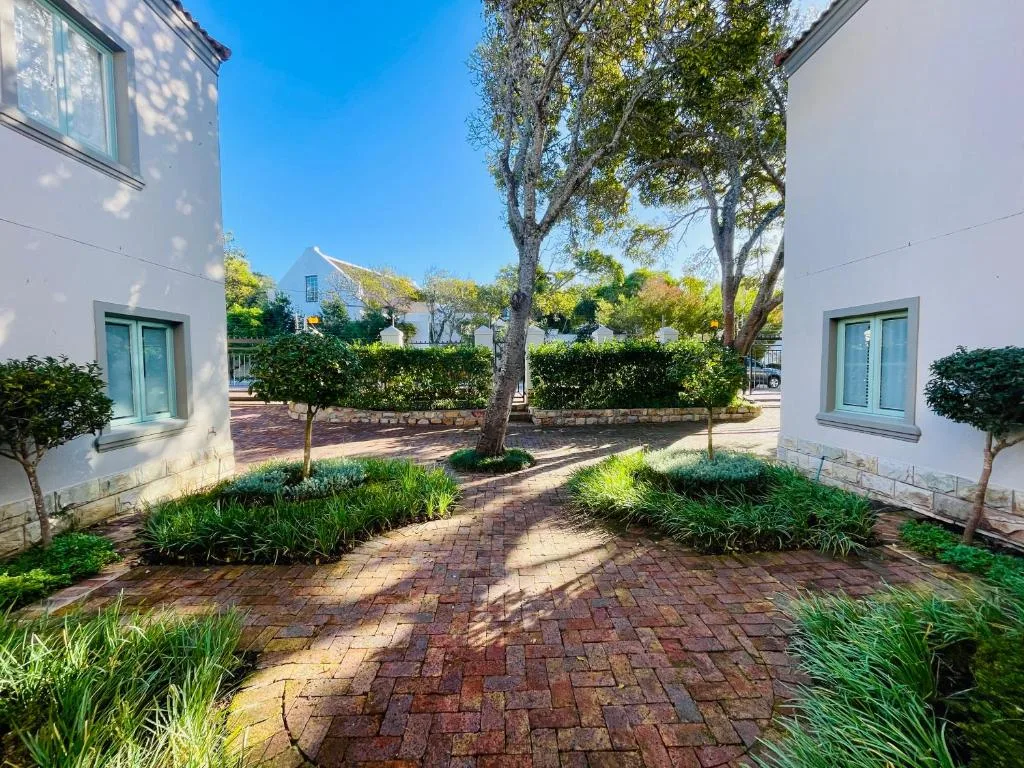 Whitewashed villa courtyard with brick paving, mature trees, and hedges