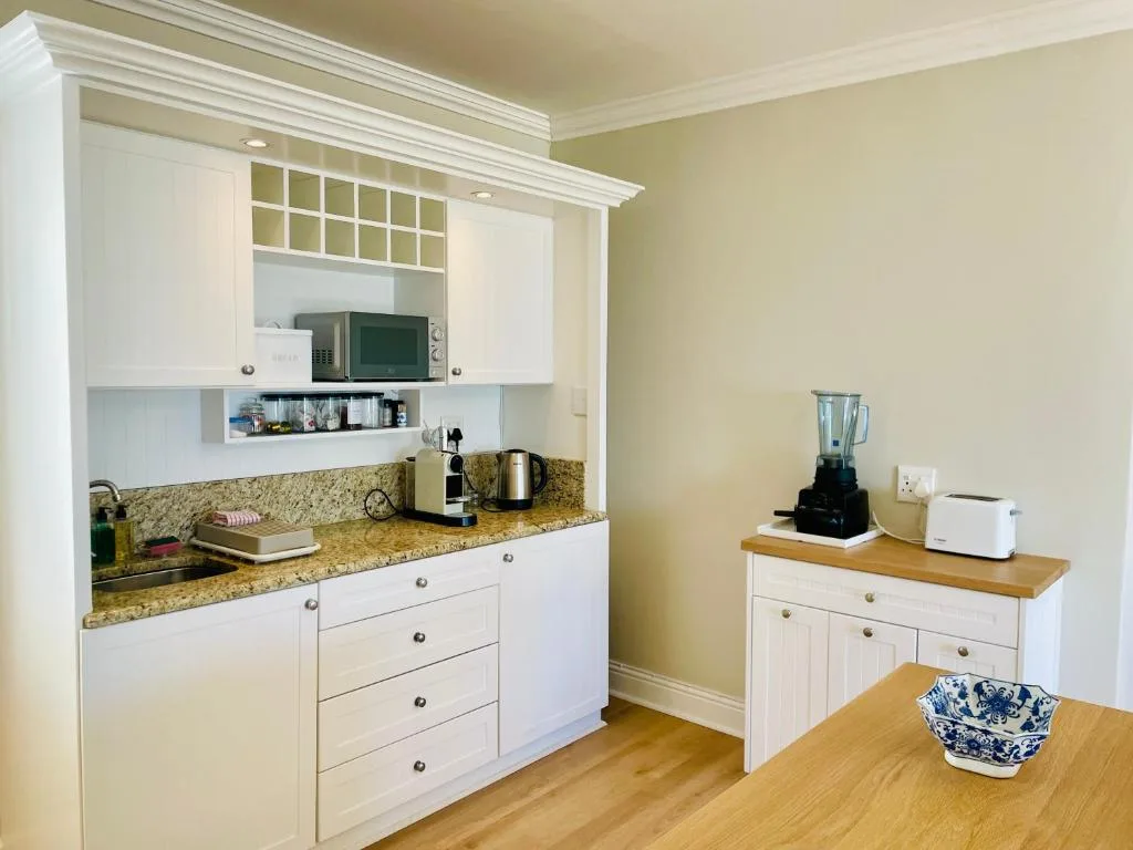 Modern kitchenette with white cabinetry, granite countertops, microwave, and appliances