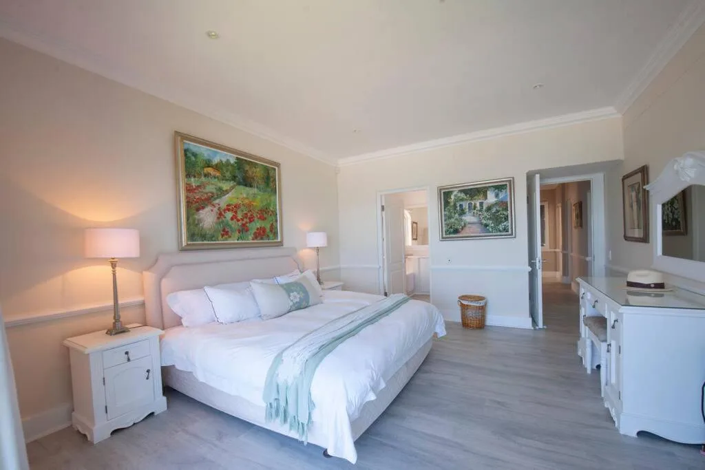 Spacious bedroom with queen bed, white furniture, and landscape artwork