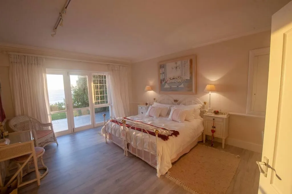 Spacious bedroom with white metal bed frame, cream linens, garden views
