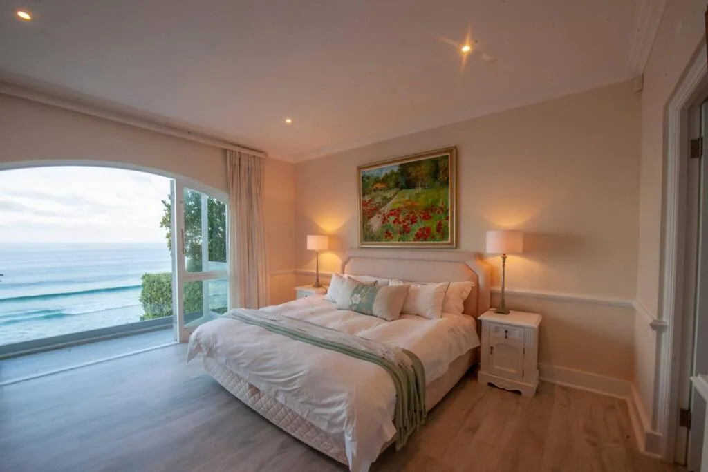 Spacious bedroom with ocean view through sliding glass doors and bedside lamps