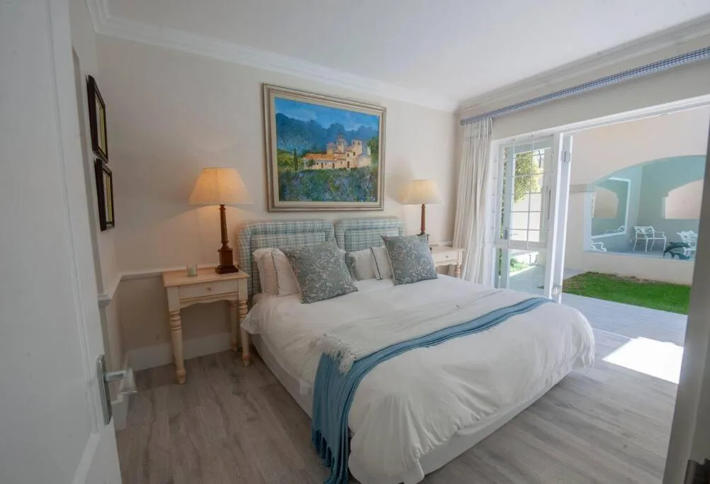 Bright bedroom with queen bed, side tables, lamps, and garden view doors