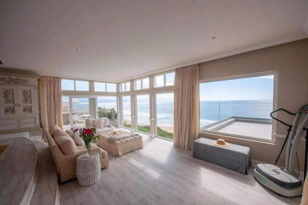 Spacious lounge with ocean views through floor-to-ceiling windows and coastal deck access