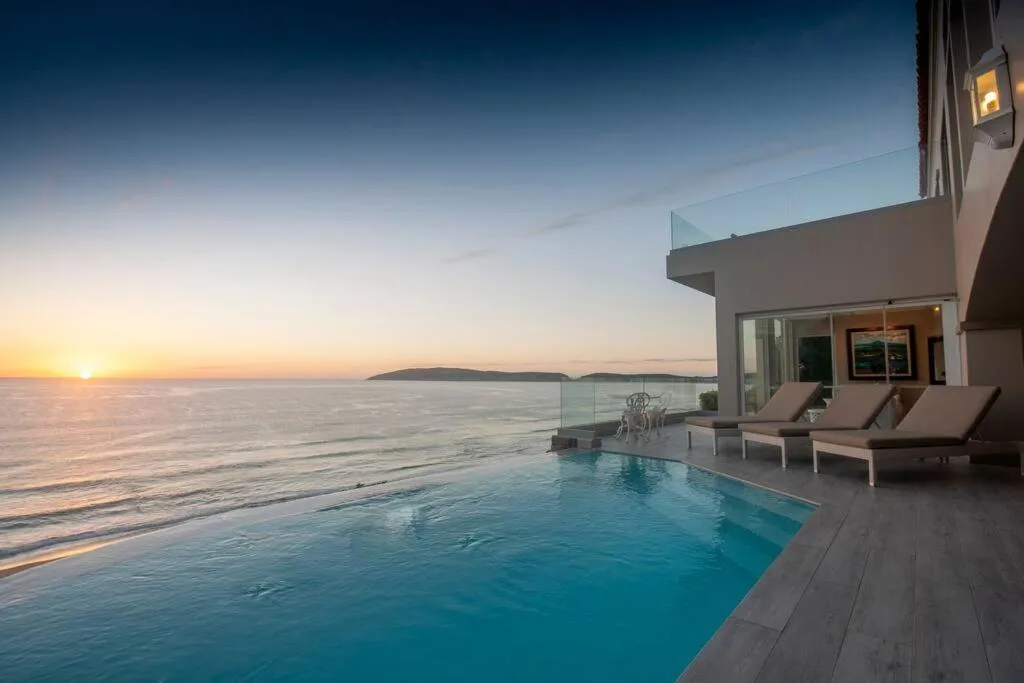 Infinity pool overlooking ocean sunset with loungers and modern deck
