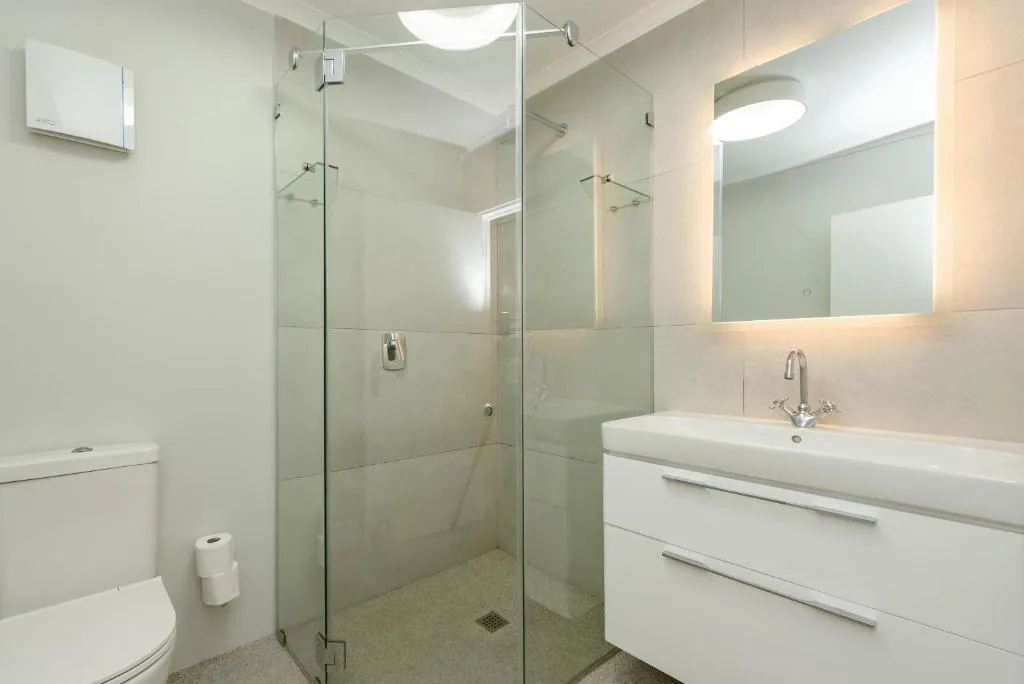 Modern bathroom with glass shower enclosure, white vanity, and illuminated mirror