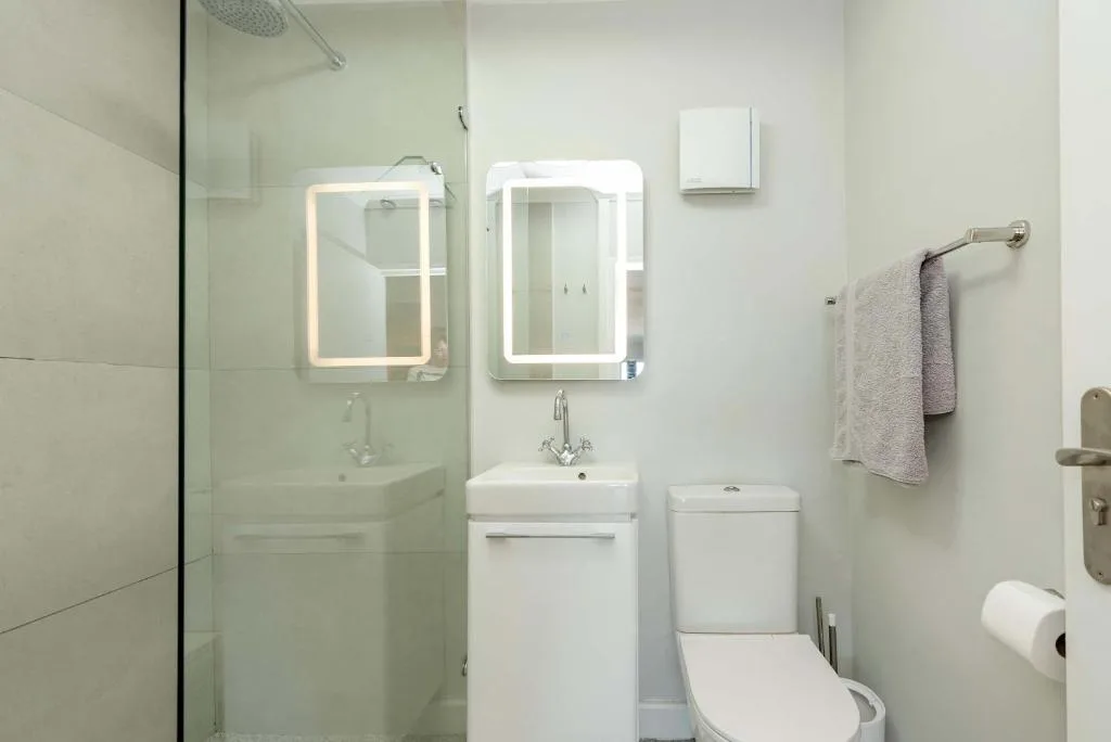 Modern bathroom with glass shower, dual illuminated mirrors, and white fixtures