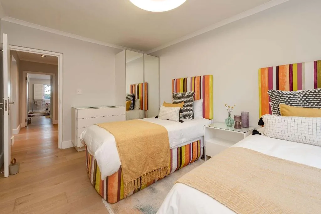 Bright modern bedroom with multiple beds, colorful artwork, and mirrored wardrobe