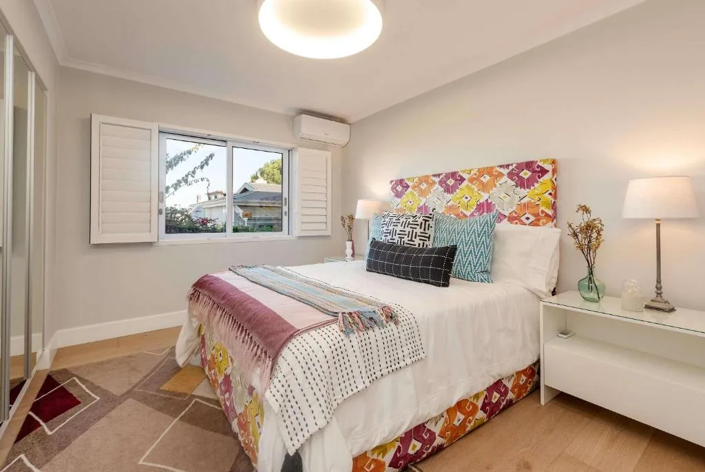 Bright bedroom with queen bed, colorful pillows, and garden views through windows