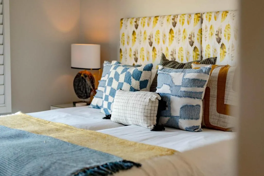 Styled bedroom with patterned pillows, leaf-print curtains, and bedside lamp