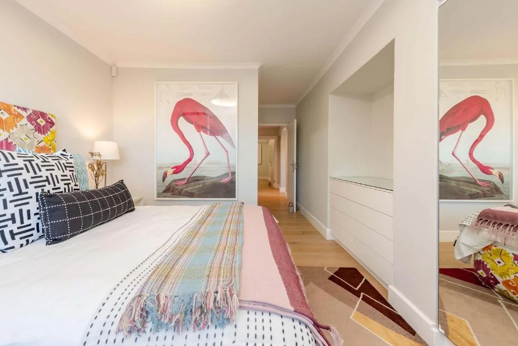 Modern bedroom with queen bed, flamingo artwork, and wooden flooring throughout