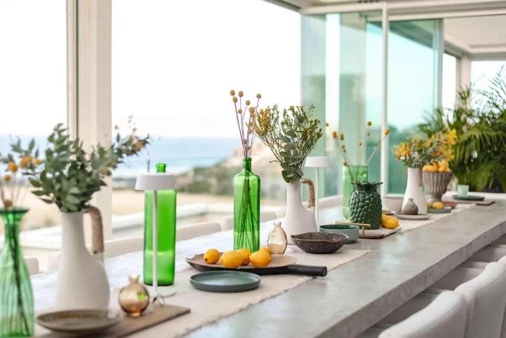 Decorative windowsill arrangement with flowers, vases, and ocean view beyond