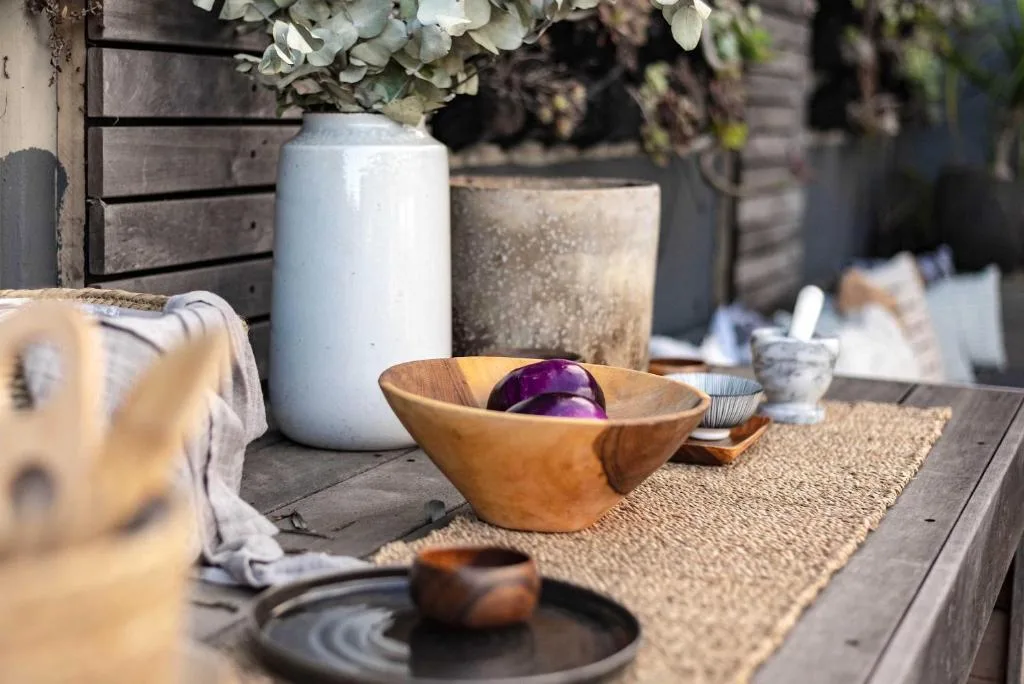 Wooden bowl with purple fruit on outdoor deck with decorative vases