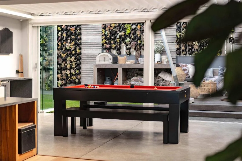 Modern lounge with black pool table and sliding glass doors opening to deck