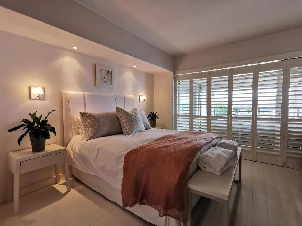 Modern bedroom with queen bed, neutral tones, warm lighting, and shuttered doors