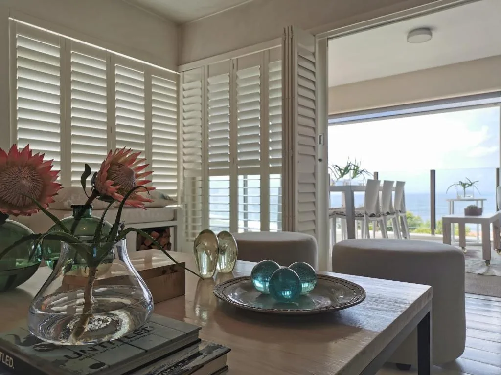 Bright lounge with shutters, flowers, ocean view through glass doors