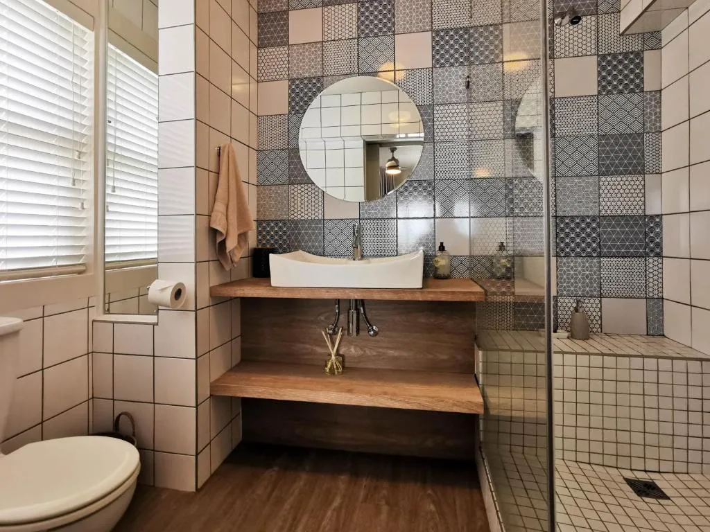 Modern bathroom with patterned tile wall, wooden vanity, round mirror, and shower