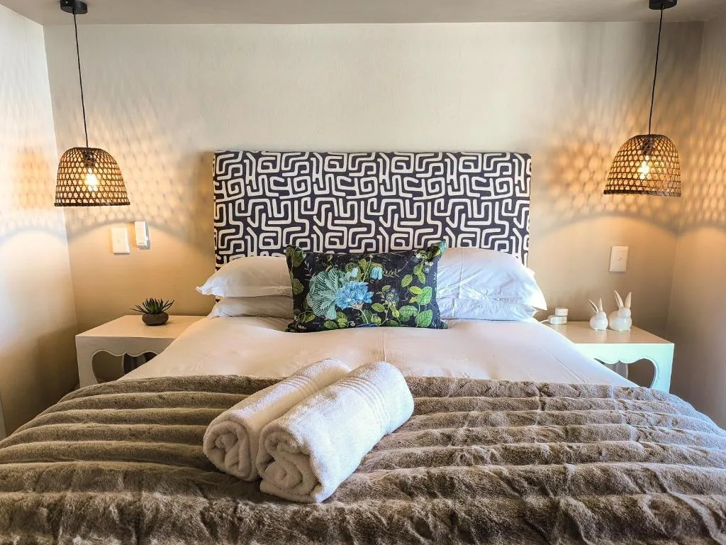 Modern bedroom with patterned headboard, pendant lights, and rolled towels
